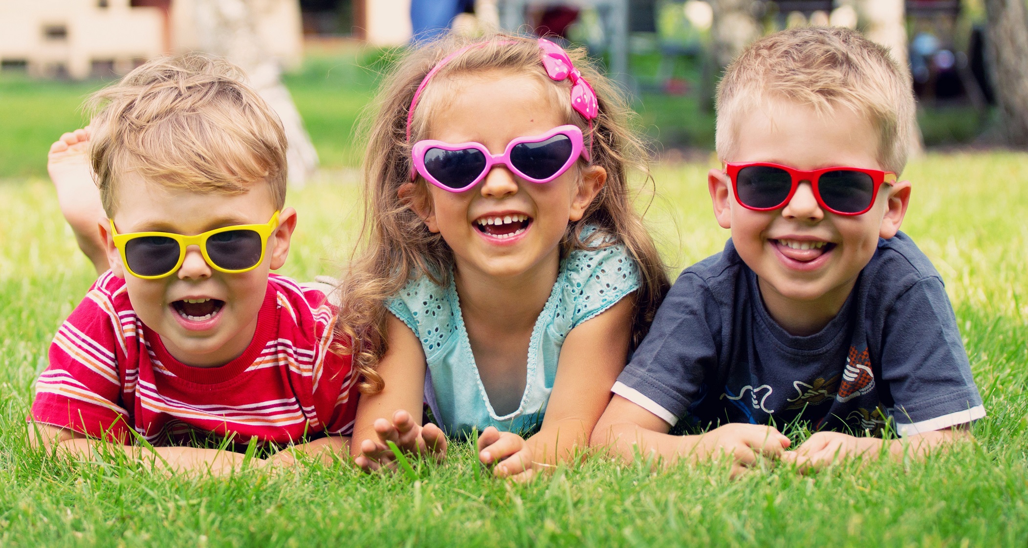Image of three children laying on the grass wearing sunglasses for UV protection.